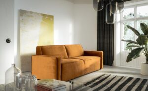 Kubiczna sofa muto w musztardowym kolorze na tle ściany z obrazem w minimalistyczny salonie.